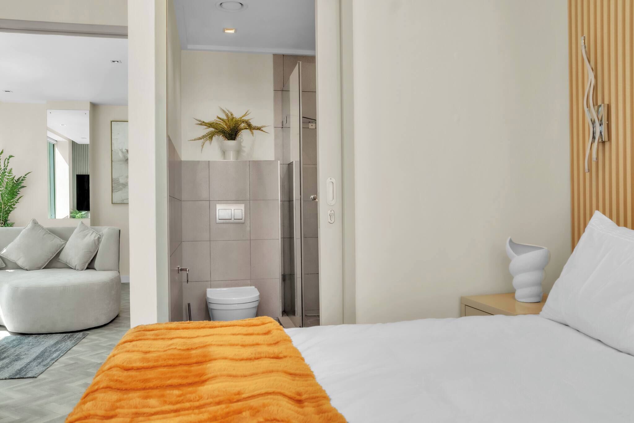 Una camera d'albergo moderna con un letto, un comodino, un bagno con doccia e un'area salotto con divano.