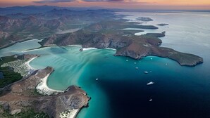 Vista aérea de uma área costeira com águas turquesa cristalinas, terreno rochoso e vários barcos.