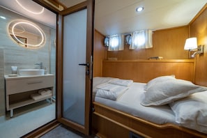 A bedroom with a wooden headboard, a bedside table with a lamp, a mirror, and a bathroom with a sink and towel rack. - Sun-Kissed Sailing Adventure in Split, Croatia (Split)