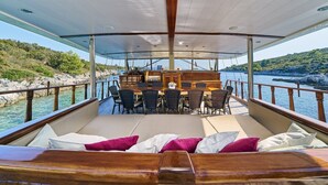 A boat deck with a dining area, seating, and a view of the coastline. - Sun-Kissed Sailing Adventure in Split, Croatia (Split)