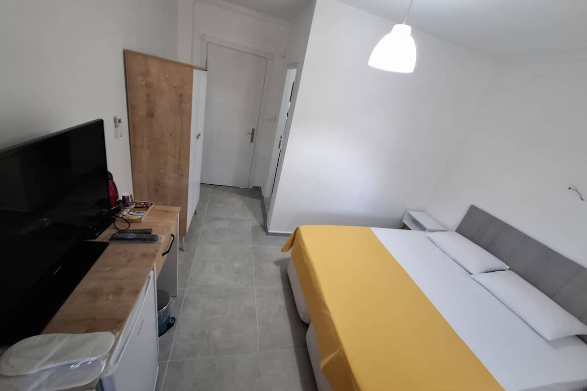A compact room with a bed, a desk, a television, and a hanging light fixture.