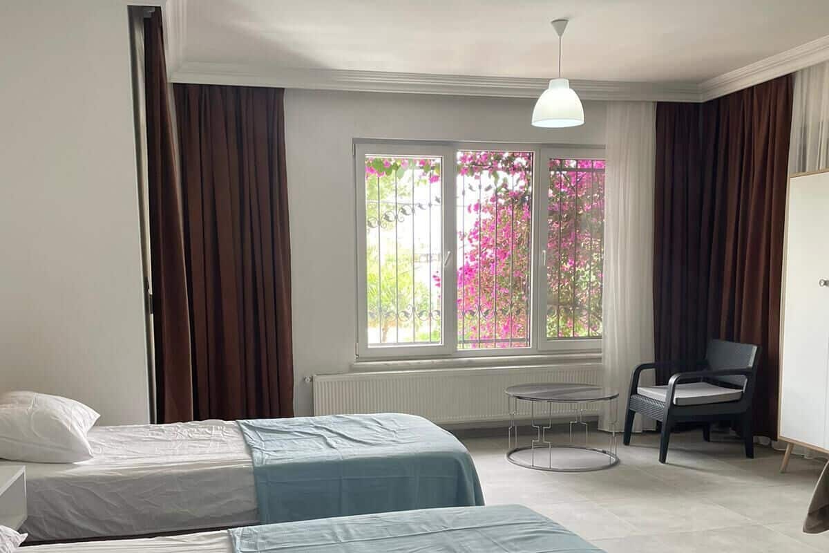 A hotel room with two beds, a chair, a desk, and a window with curtains.