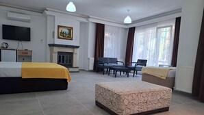 Habitación de hotel con cama, sofá, sillón, mesa, chimenea, televisor y ventanas amplias.