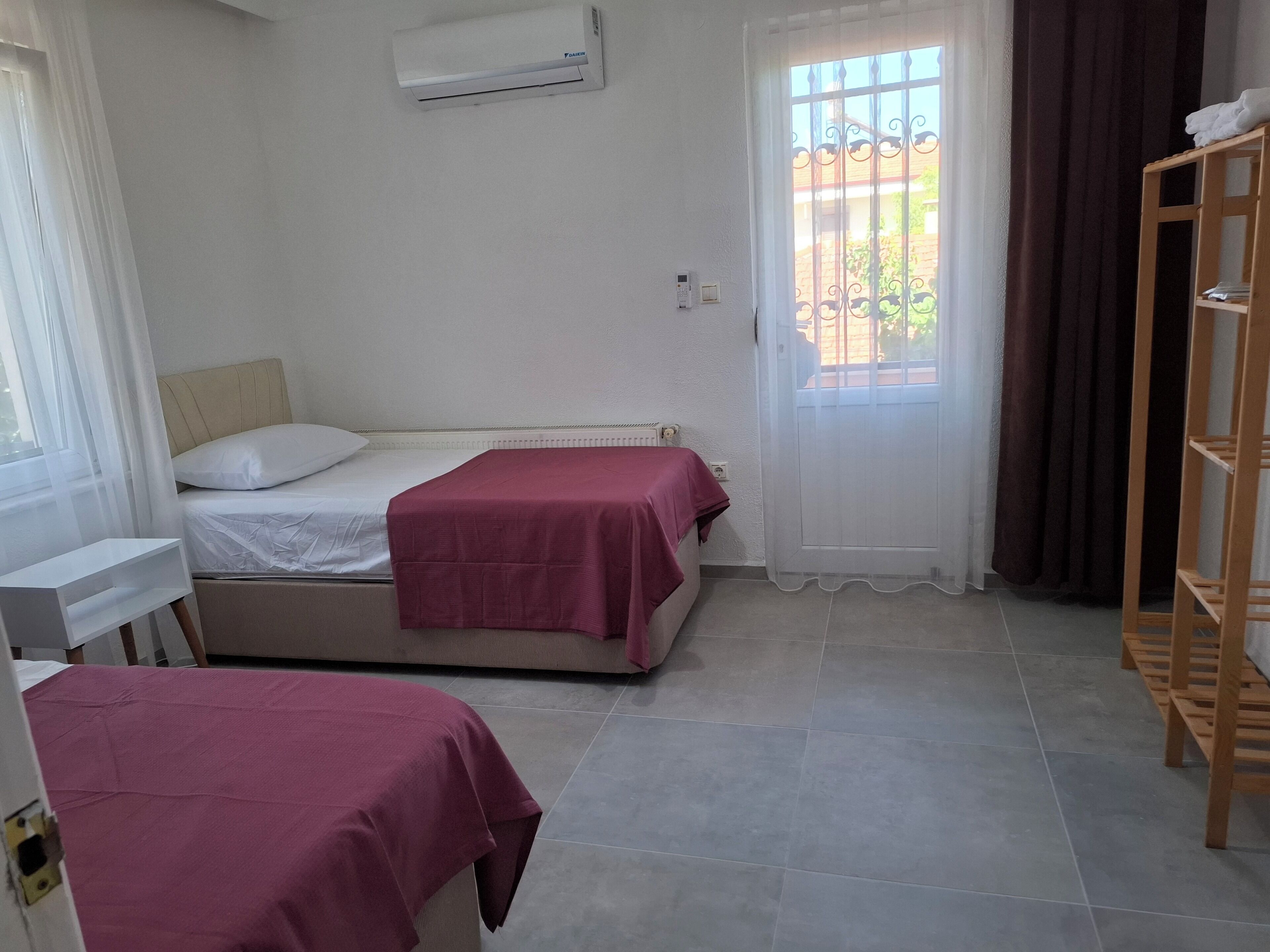 Een kamer met twee bedden, een raam met gordijnen, een airconditioning en een houten plank.