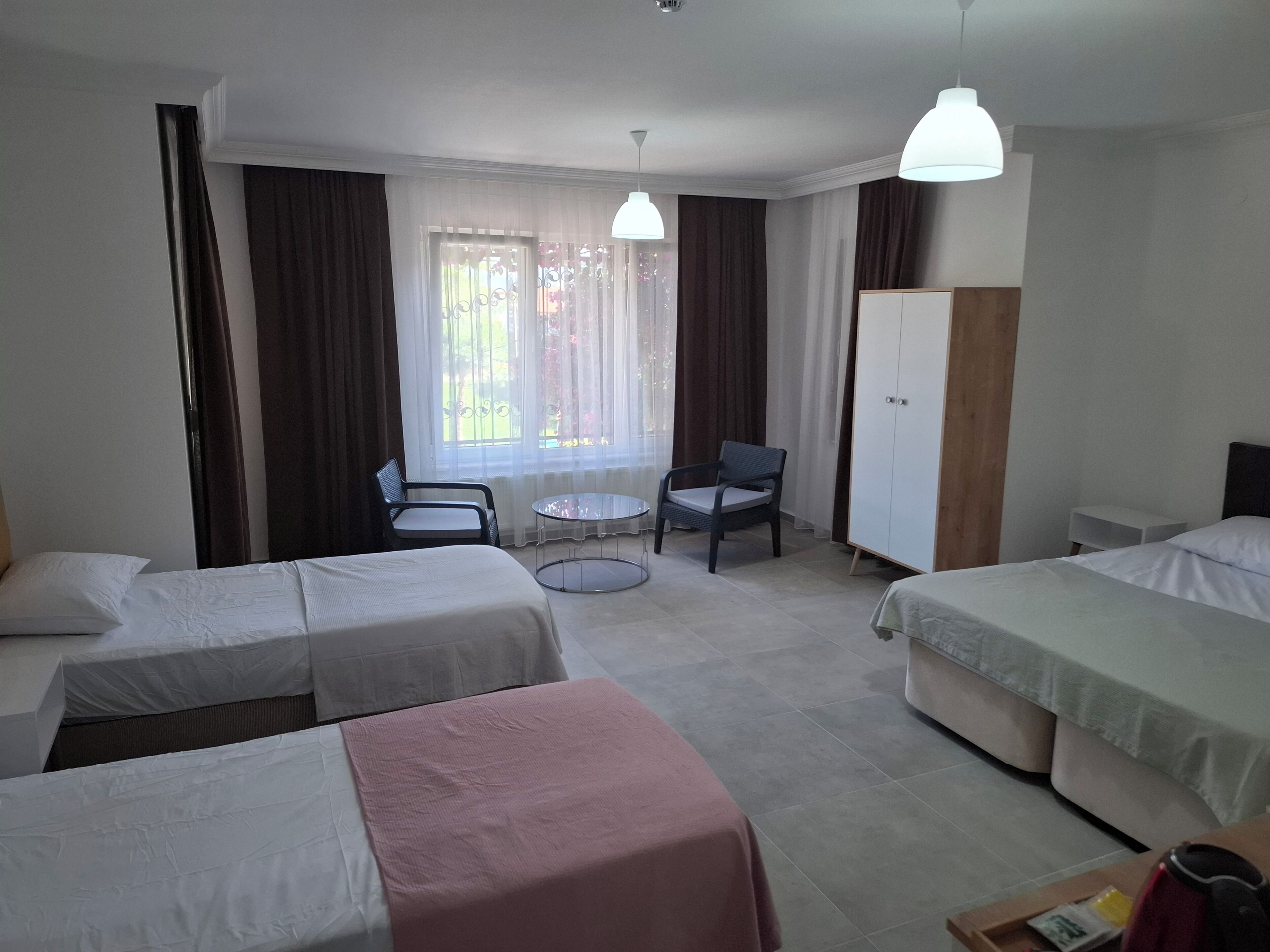 A hotel room with two single beds, a small round table, a chair, a wardrobe, and a window with curtains.