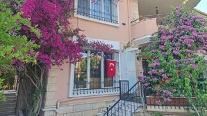 Un edificio de dos pisos con balcón, una bandera y plantas con flores.