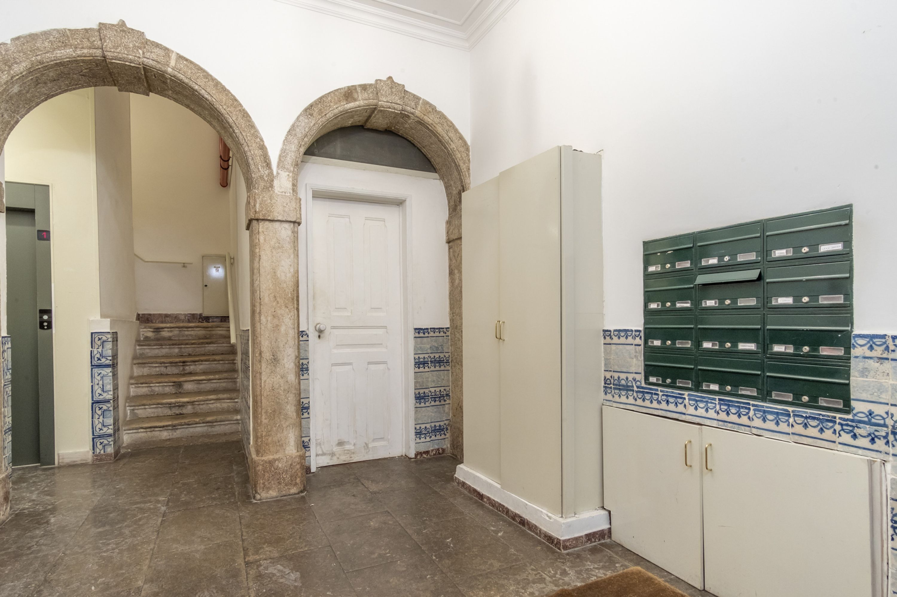 Ein Flur mit einer weißen Tür, einer Treppe und einem grünen Aktenschrank.
