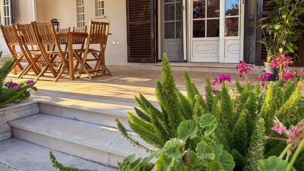 Une terrasse avec une table et des chaises, une porte-fenêtre coulissante et un jardin agrémenté de plantes et de fleurs.