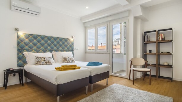Un dormitorio con cama, una silla, una estantería y una ventana.