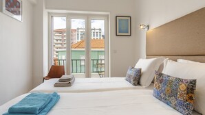 Habitación de hotel con cama, una silla, balcón y vistas a edificios.
