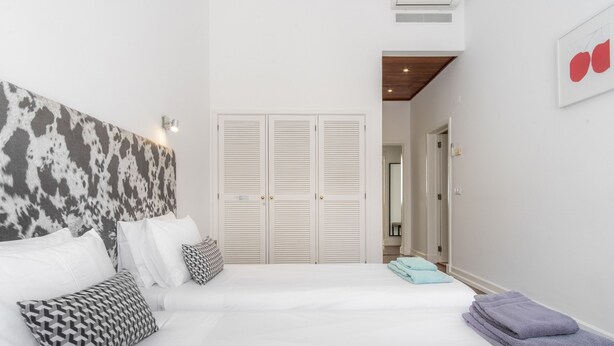 Une chambre à coucher avec un lit, des oreillers, une tête de lit, une armoire et une salle de bain visible à travers une porte ouverte.