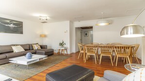 Una sala de estar moderna con sofá, mesa de centro, mesa de comedor con sillas e iluminación colgante.