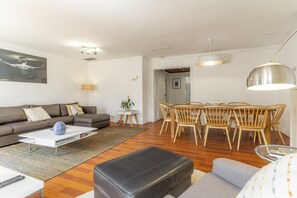 Ein modernes Wohnzimmer mit Sofa, Couchtisch, Esstisch mit Stühlen und Pendelleuchten.