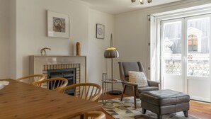 Un comedor con una mesa y sillas de madera, una chimenea, un sillón gris con cojín y una alfombra estampada.
