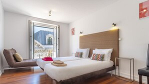 Habitación de hotel con dos camas, un sofá, una mesita y vista a un edificio a través de una ventana.
