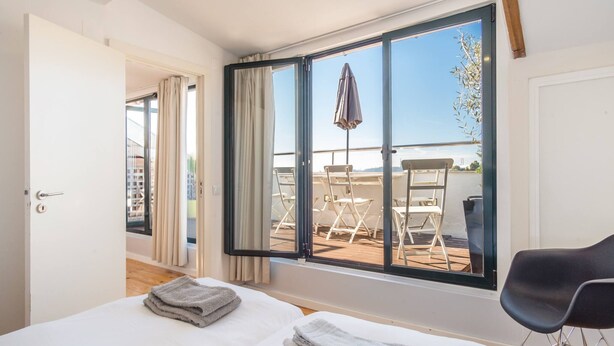 Habitación de hotel con cama, una silla, balcón con mesas y sillas, y vista al mar.