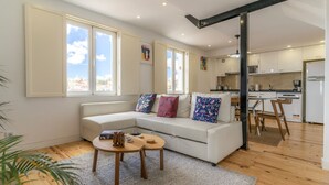 Una sala de estar moderna con un sofá blanco, una mesita de centro de madera y vistas de la ciudad a través de amplias ventanas.