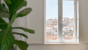 Una ventana con vista a un paisaje urbano, una planta en primer plano y una pared blanca.