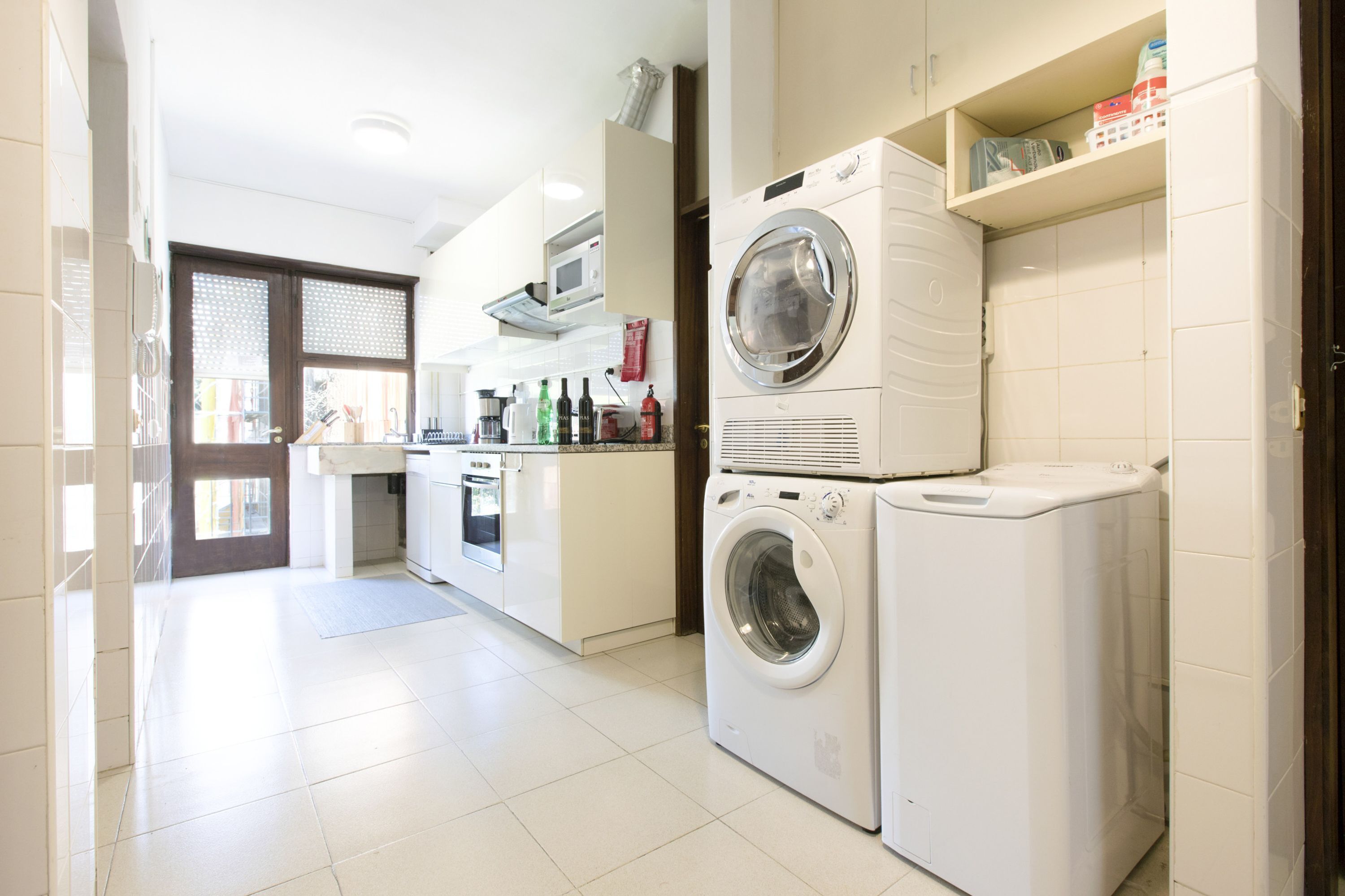 A laundry area with a washing machine, dryer, microwave, and a small kitchen area with a sink and countertop.