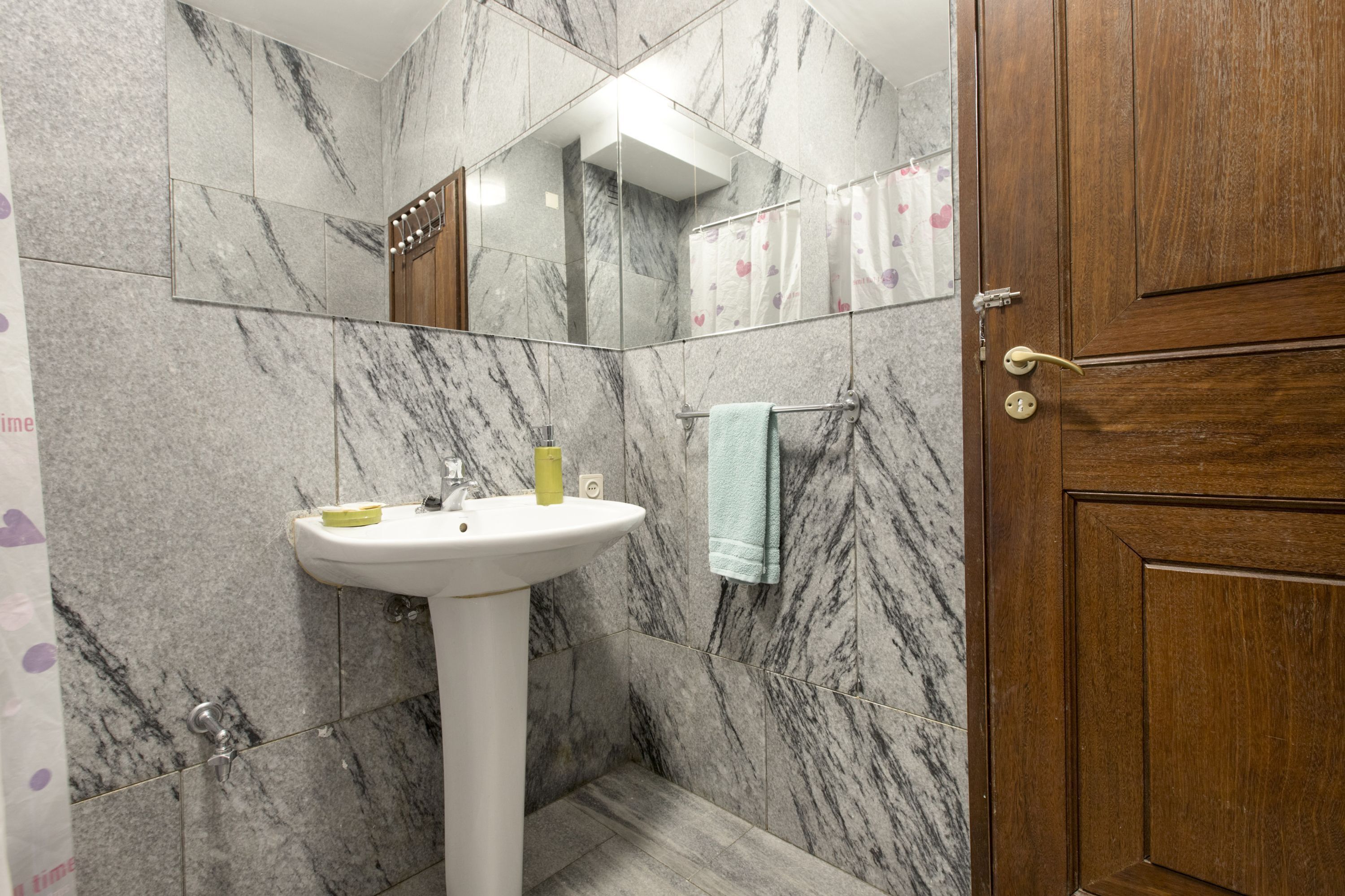 A bathroom with a marble wall, a sink, a mirror, and a wooden door.