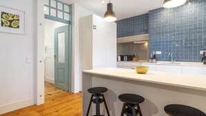 Eine moderne Küche mit weißer Arbeitsplatte, blauer Spritzschutzwand und zwei schwarzen Barhocker.