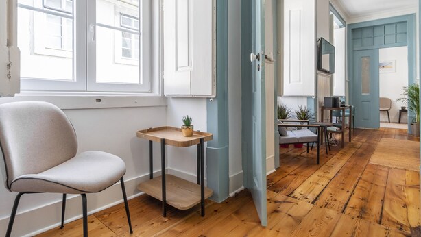 Ein Zimmer mit Holzboden, einem Sessel, einem kleinen Tisch mit Pflanze und einer Tür zu einem anderen Raum.