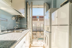 Cozinha pequena com pia, máquina de lavar e vista para uma varanda com telhado em azulejos.