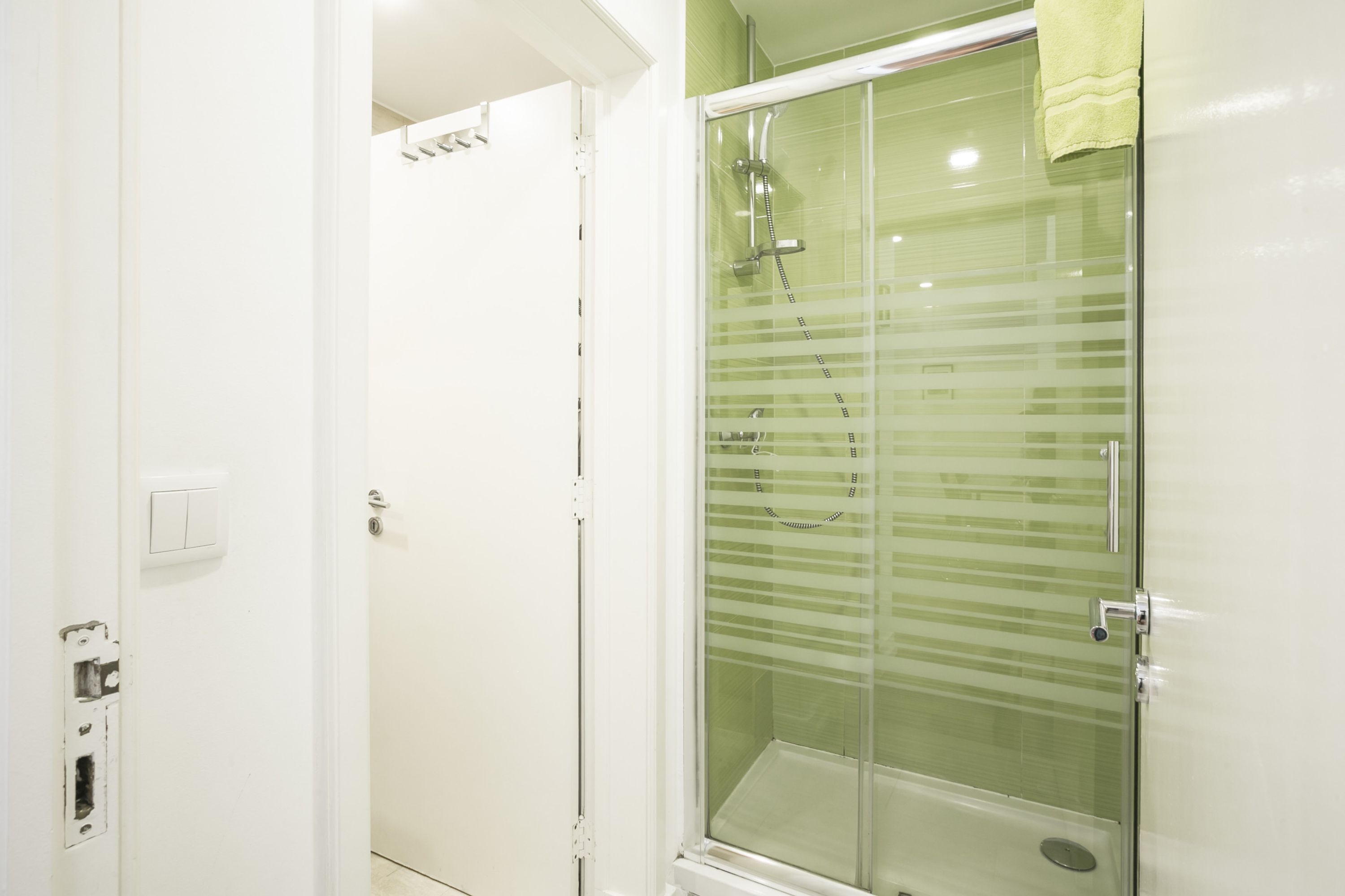 Un baño con cabina de ducha de vidrio, una puerta blanca y una toalla colgada en la puerta de la ducha.