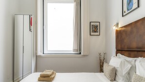 A hotel room with a bed, a wardrobe, a window, and a wall-mounted light fixture. - CH8 in Lisboa Ciudad (Lisbon)