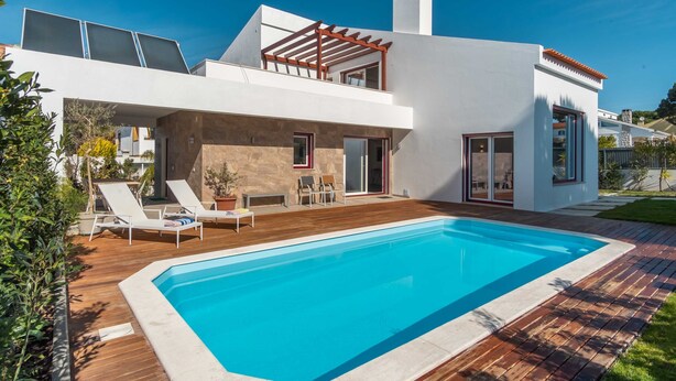 Een modern huis met een zwembad, een overdekt terras en een gevel van natuursteen.