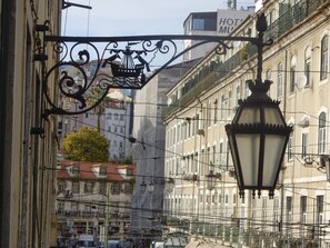 A street view with a hanging black wrought iron lamp, a sign for 'HOTEL MU' above a building, and a 'PRACA ECOLI' sign below. - FI in Lisboa Ciudad With 2 Bedrooms and 1 Bathrooms (Lisbon)