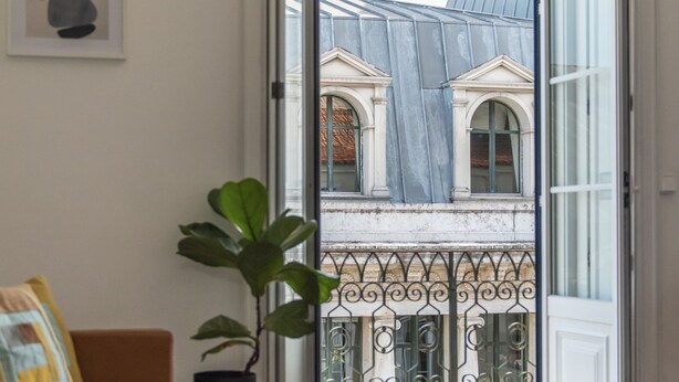 A room with a sofa, a table, a potted plant, and a view of buildings through an open door. - CH1 in Lisboa Ciudad (Lisbon)