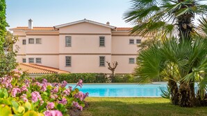 Un edificio grande con piscina, rodeado de vegetación y palmeras.