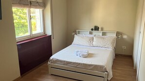 Quarto com uma cama, janela com cortinas, ar condicionado branco e chão de madeira.