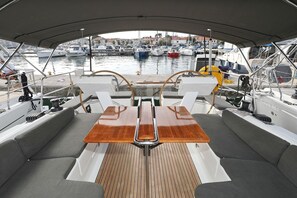 A boat's deck with a central table, cushioned seating, and a view of the marina.