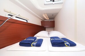 Ein schmales Blockhäuschen mit einem Bett, zwei Handtüchern, einem Fenster und einer Duschbrause.