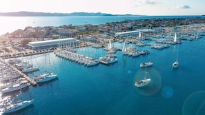 Ein Yachthafen mit vielen vor Anker liegenden Booten, ein modernes Gebäude und eine Küstenstadt im Hintergrund.