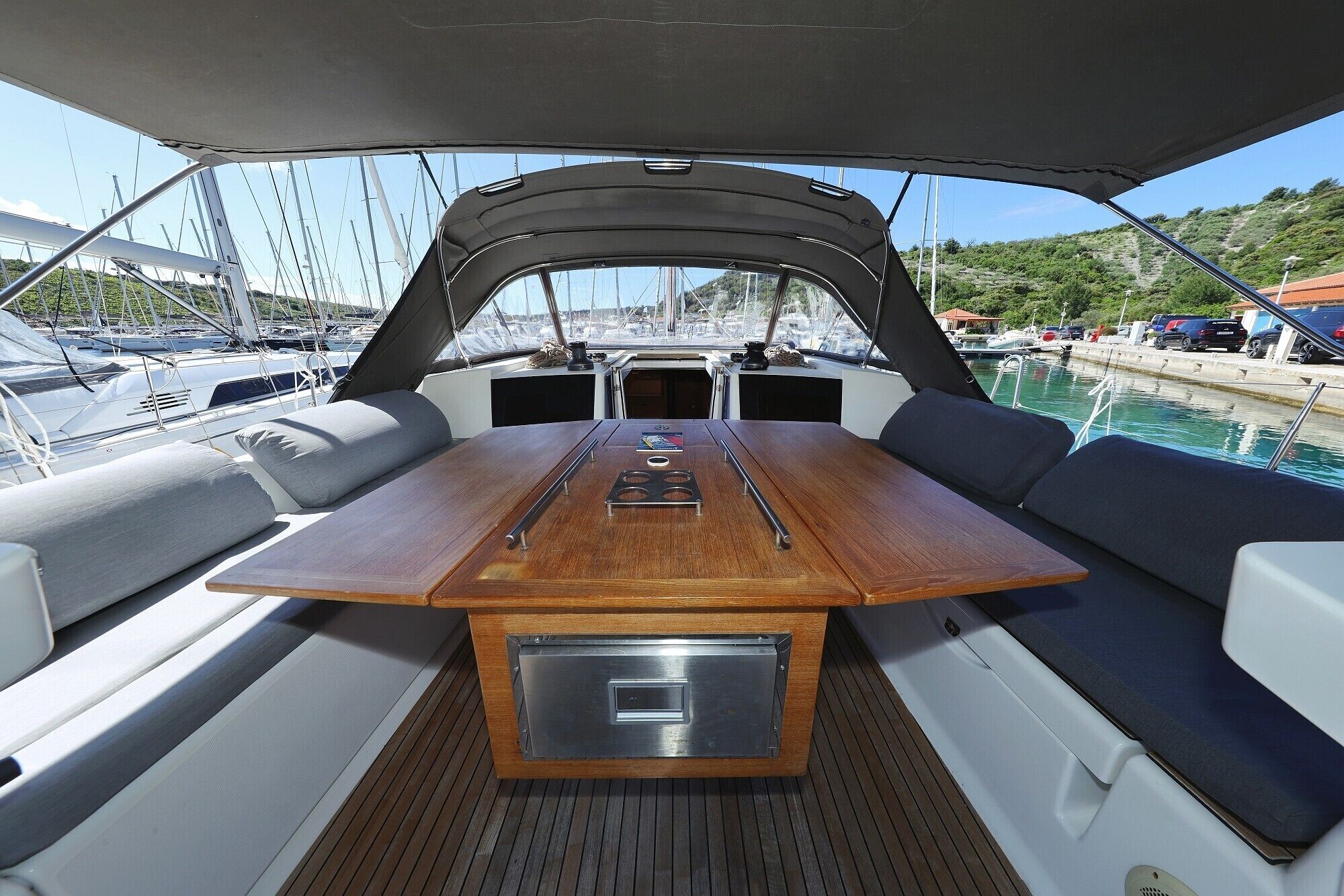 Das Deck eines Bootes mit einem zentralen Tisch, gepolsterten Sitzgelegenheiten und Blick auf den Yachthafen.