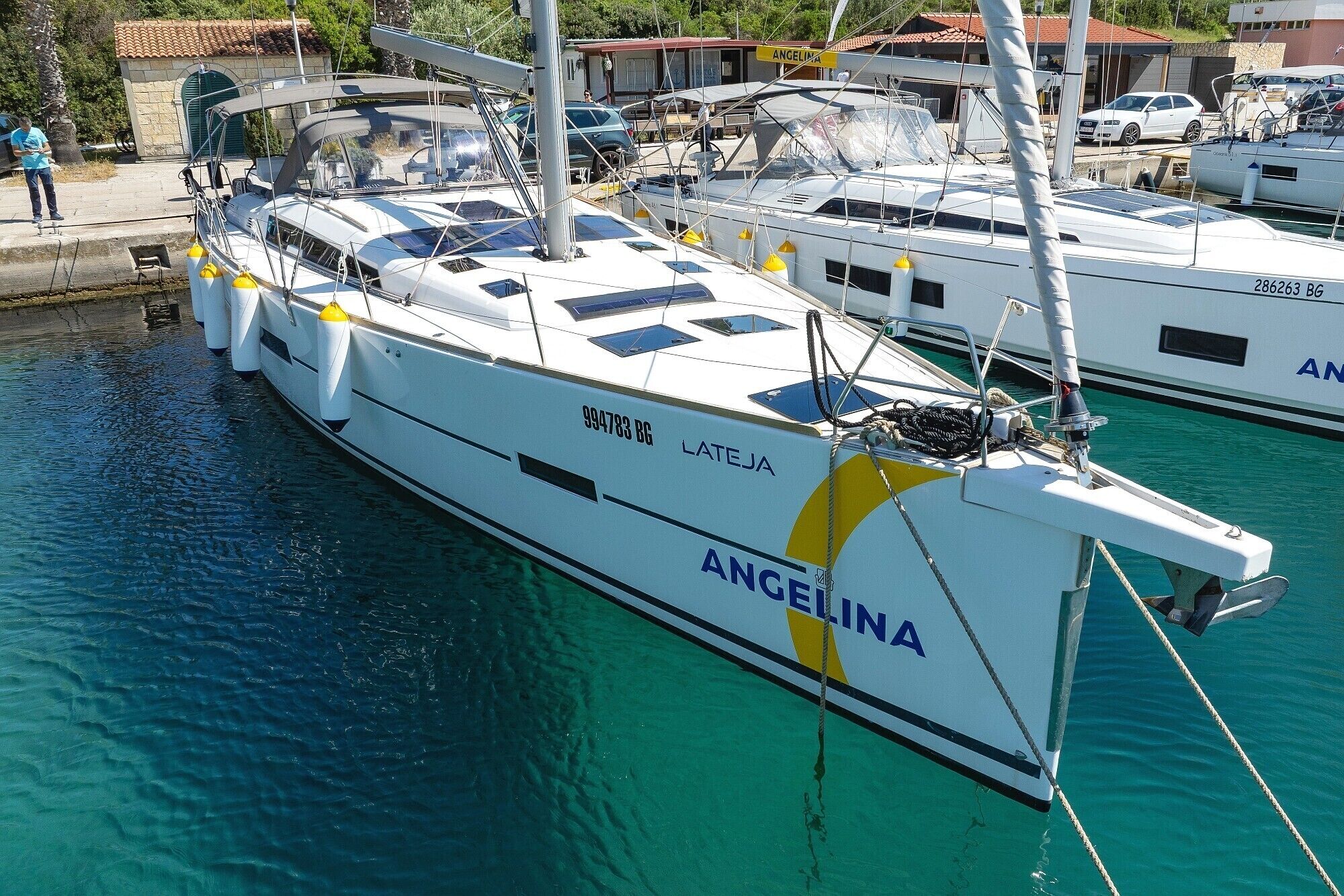 Un port de plaisance où sont amarrés de nombreux yachts, dont l’un porte les inscriptions « LATEJA » et « ANGELINA ».