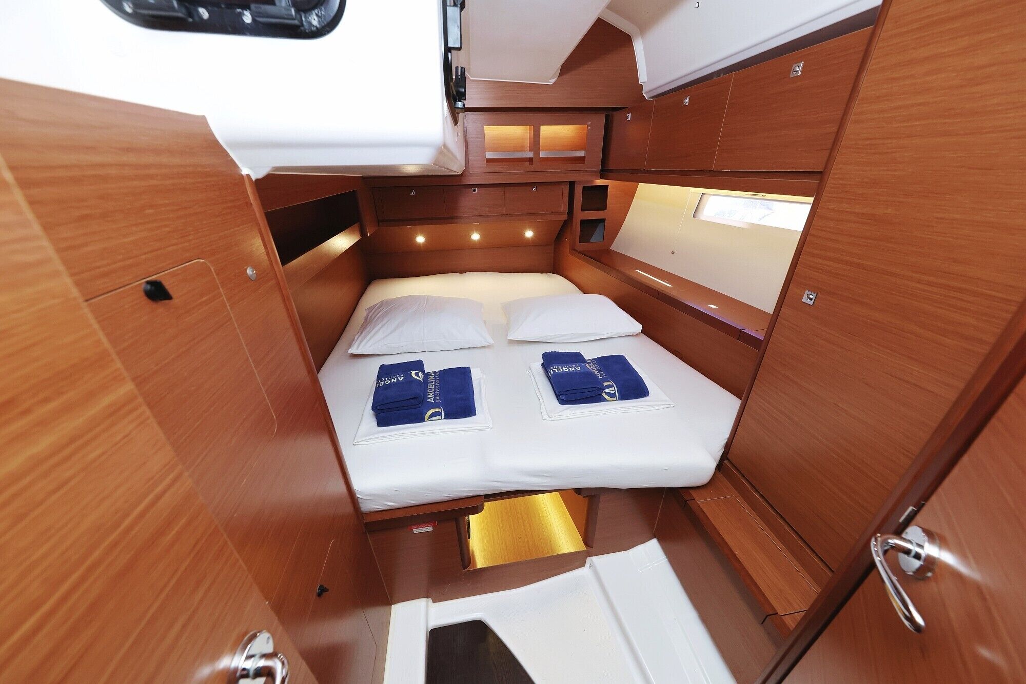 Une cabine compacte et bien éclairée, avec un lit simple, un lambris en bois et une petite fenêtre.