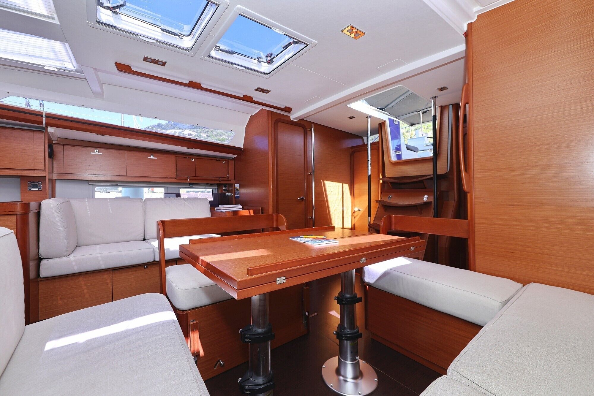 A boat interior with a dining table, cushioned seating, and a small kitchen area.