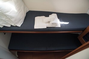 A single bed with a dark mattress and a white pillow, a rolled white towel, and a folded white towel on the bed. - Sun-Kissed Sailing Adventure in the Ionian Islands, Lefkada (Lefkada)