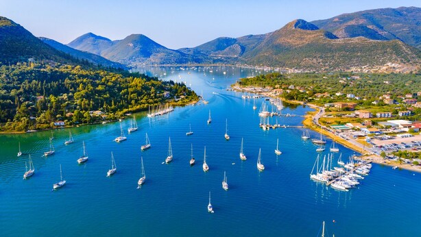 A marina with numerous sailboats docked, surrounded by lush green hills and mountains.