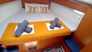 A compact cabin with a single bed, two pillows, a small table with towels, and a window.