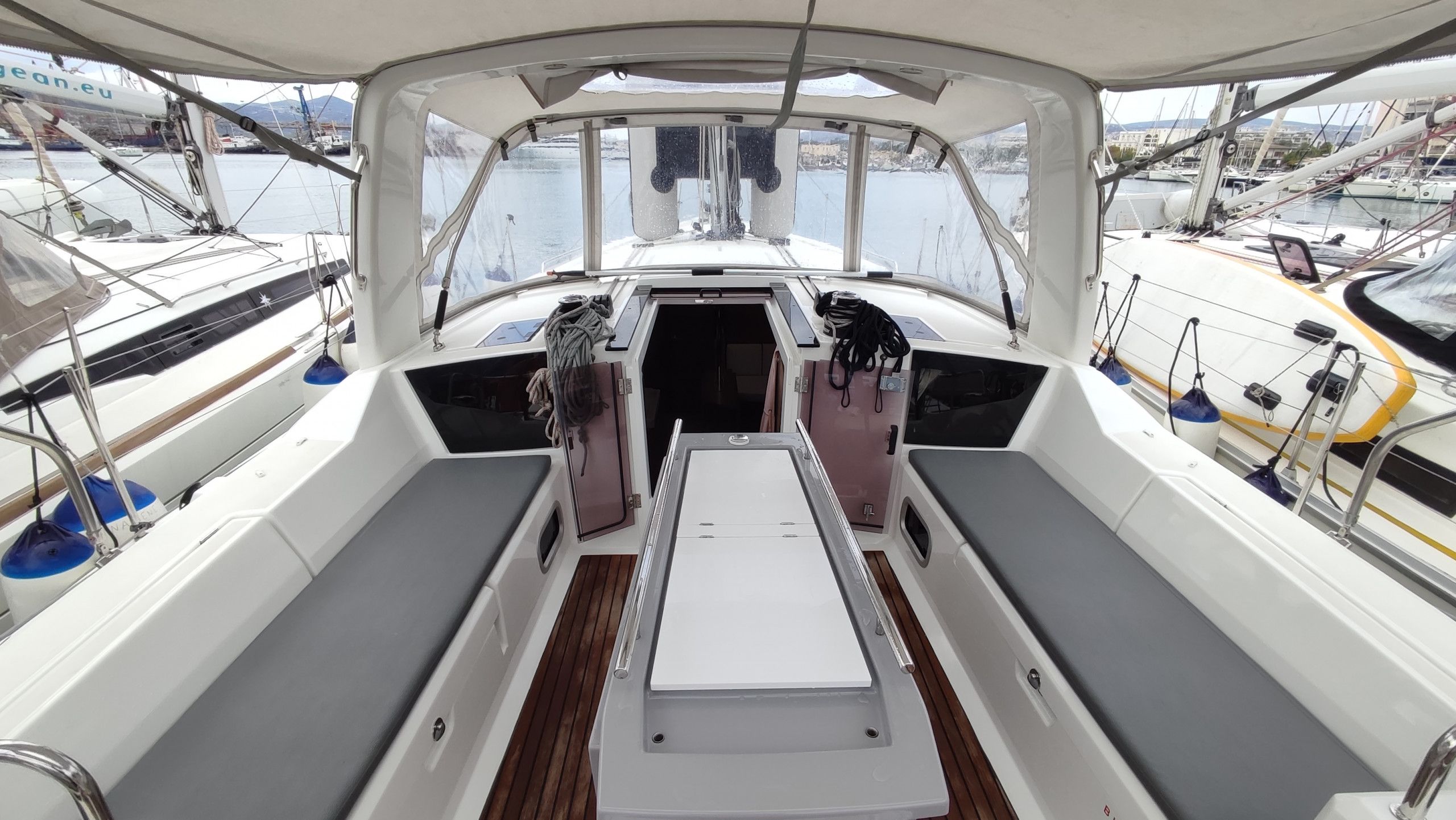 Cubierta de barco con zona de estar central, ventanas laterales y vista al puerto deportivo.