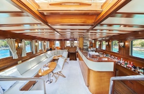 Interior de barco com bar, área de estar e amplas janelas.