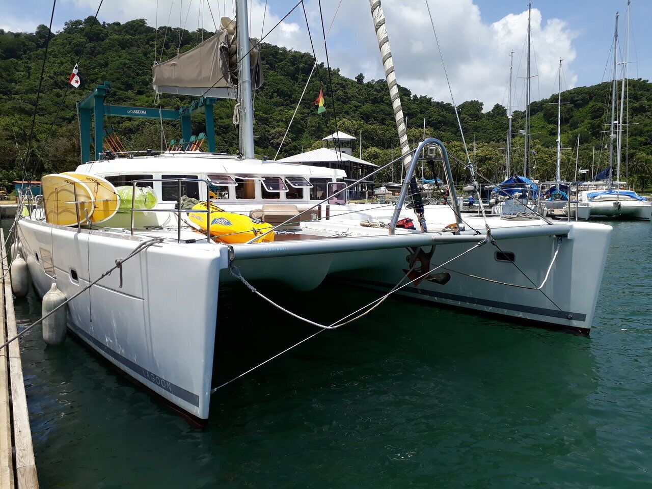 Un yate blanco amarrado en un puerto deportivo con una colina boscosa al fondo.