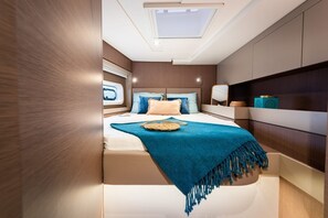 Une chambre avec un puits de lumière, un lit recouvert d’une couverture bleue et une table de chevet agrémentée d’objets décoratifs.