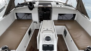 Interior de un barco con un panel de control central, dos zonas de asiento acolchadas y cubierta de madera.
