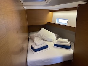 Ein kleines Bett mit weißer Bettwäsche und gefalteten Handtüchern in einer Holzhütte mit einem kleinen Fenster.